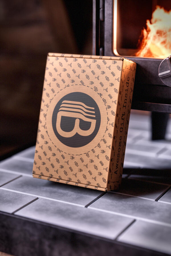 A patterned rectangular Kraft gift box with a circular 'B' logo, resting on a tiled surface near a lit fireplace.