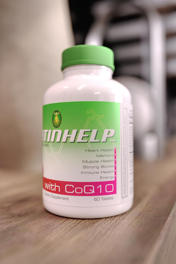 A white bottle of Statinhelp dietary supplement with a green cap and label, highlighting CoQ10 content and health benefits, on a wooden table.